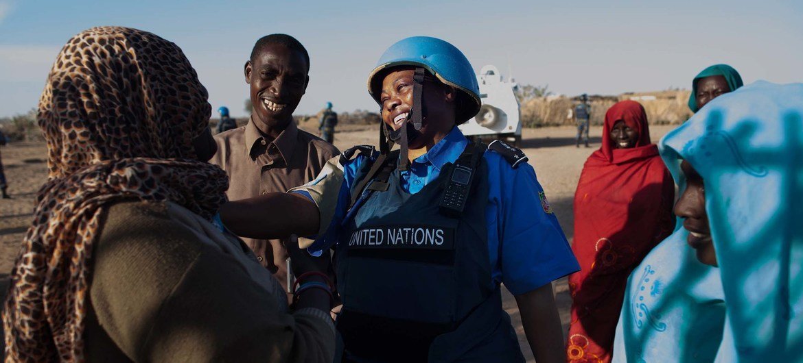 A UNAMID police officer in a blue helmet and vest labeled 'UNITED NATIONS' interacts with women at a water point in Nifasha camp, north Darfur.