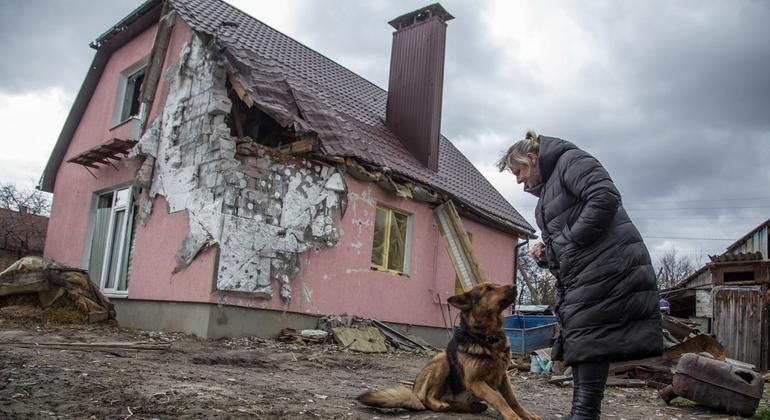 Une femme ukrainienne avec son chien se tient près d'une maison endommagée.