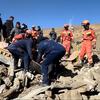 Firefighters in orange and blue uniforms search through rubble at the site of an earthquake in Tibet.