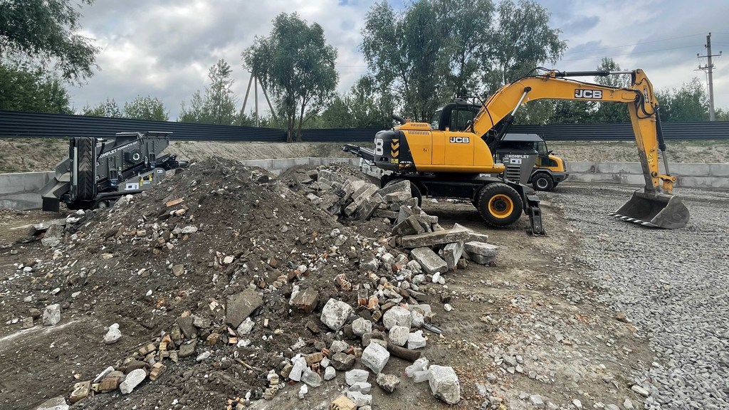 Желтый экскаватор JCB и другая тяжелая техника работают на строительной площадке в Украине, расчищая завалы и обломки поврежденных войной зданий.