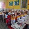 Em uma sala de aula brasileira, os alunos levantam as mãos com entusiasmo.