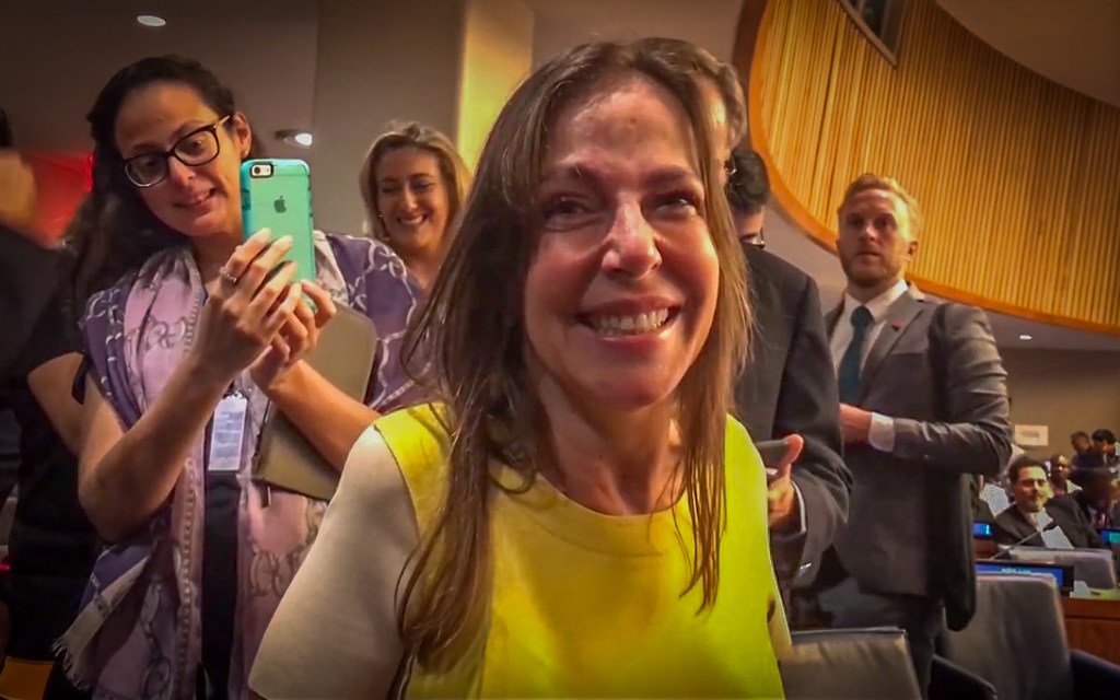 A senadora e política brasileira Mara Gabrielli sorri enquanto é fotografada por uma mulher com um smartphone em uma sala de conferências.