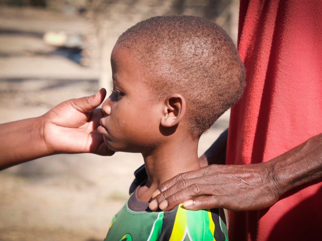Mkono wa mtu mzima umekaa begani mwa mvulana mdogo wa Msumbiji, huku mkono mwingine ukimgusa usoni kwa upole.