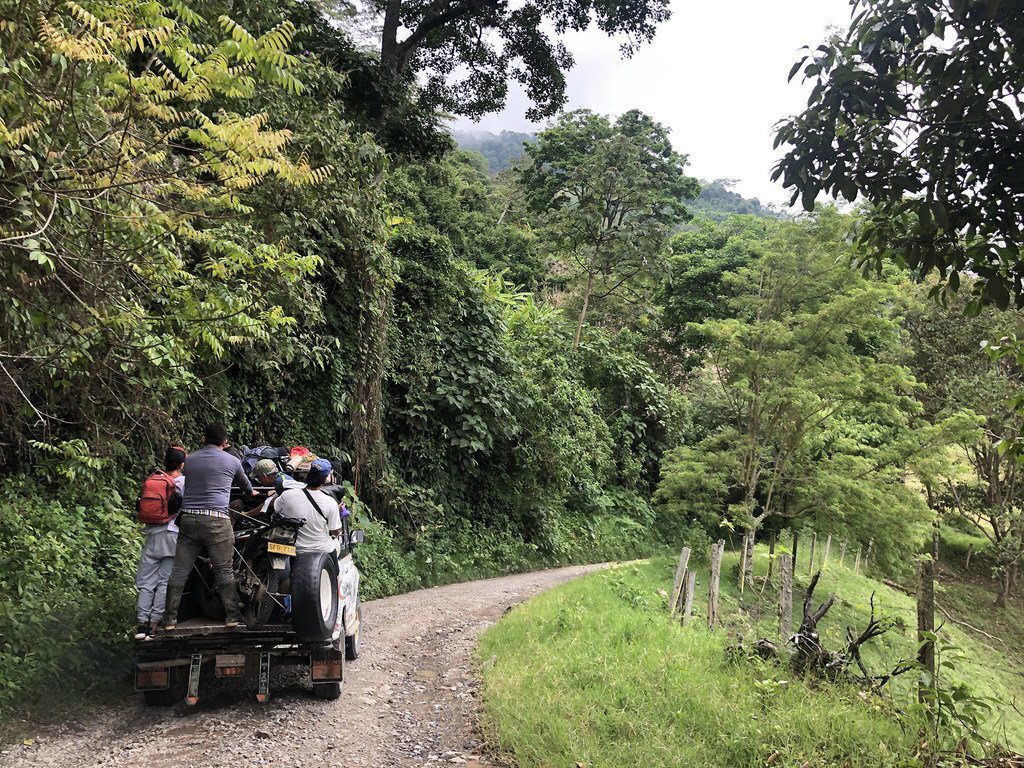 Excombatientes de las FARC-EP y lugareños viajan en la parte trasera de un vehículo todoterreno por un camino de tierra en una exuberante selva de Colombia.