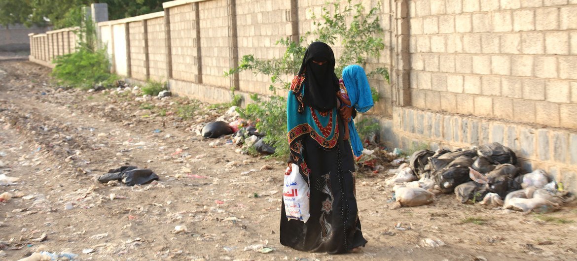 امرأة تحمل طفلها الذي يعاني من سوء تغذية شديدة ومضاعفات صحية تسير باتجاه مركز صحي في الحديدة، اليمن.