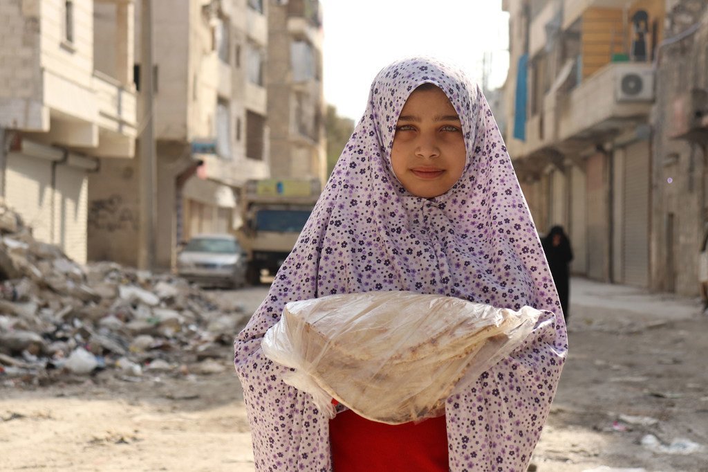 فتاة في حي الصالحين الفقير في حلب تحمل الخبز الذي يقوم بتوزيعه برنامج الأغذية العالمي