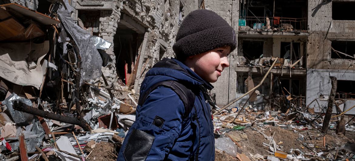 यूक्रेन के एक रिहायशी इलाक़े में एक 10 वर्षीय बच्चा अपने परिवार के घर वाली इमारत के सामने से गुज़रता हुआ. ये इमारत, एक हवाई हमले में ध्वस्त हो गई.