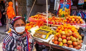 A woman works as a fruit vendor in Dhaka, Bangladesh. A single parent, she is accompanied at work by her two daughters.