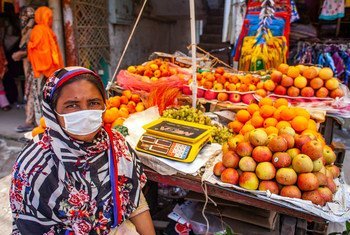 A woman works as a fruit vendor in Dhaka, Bangladesh. A single parent, she is accompanied at work by her two daughters.
