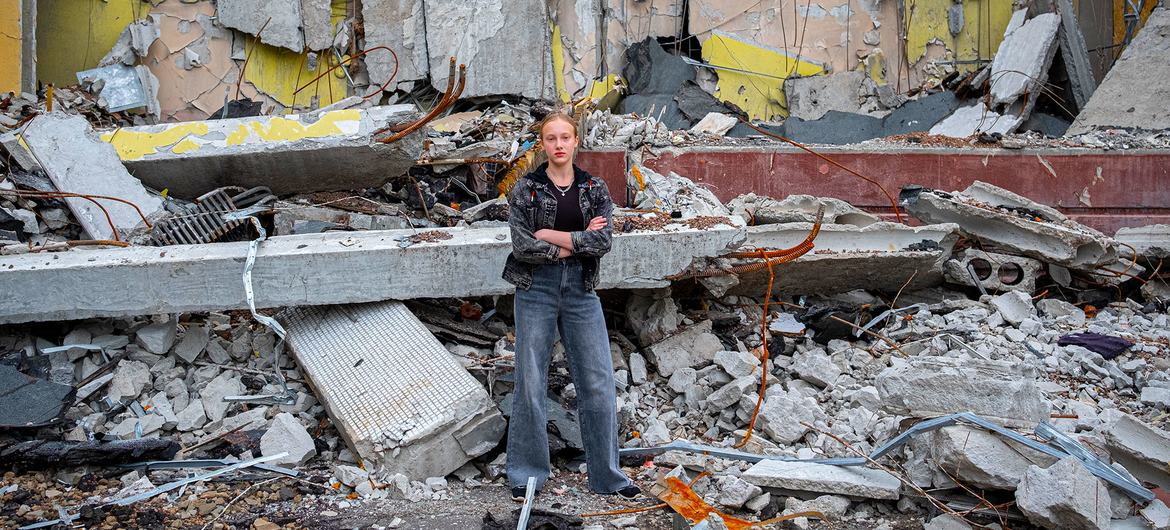 Uma menina de doze anos em frente à sua escola em Kharkiv, na Ucrânia, que foi destruída em um ataque aéreo. Agora ela vai estudar online