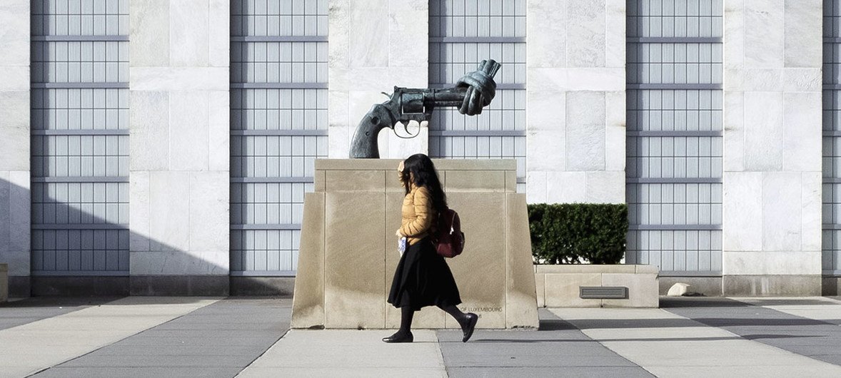 موظفة بالأمم المتحدة تدخل إلى المقر عبر مدخل الزوار. ويظهر خلفها "المسدس المعقود" الذي يرمز إلى اللاعنف.