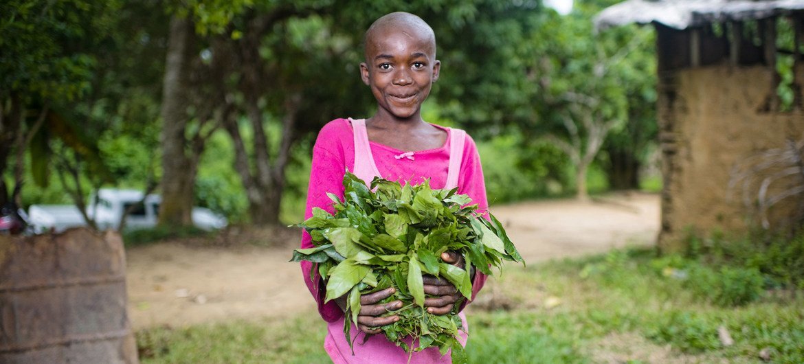 A child holds vegetables grown in her garden in a village in Cameroon.