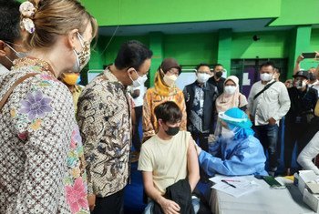 DKI जकार्ता के गवर्नर, UNHCR इण्डोनेशिया के प्रतिनिधि और KADIN (इण्डोनेशिया चेम्बर्स ऑफ कॉमर्स एण्ड इन्डस्ट्री) के सदस्यों के साथ, एक युवा शरणार्थी को टीका लगते हुए देख रहे हैं.