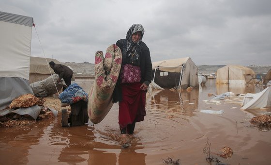 سيّدة تحاول إنقاذ حاجياتها بعد أن أغرقت الفيضانات مخيمها الواقع في شمال غرب سوريا في كانون الثاني/يناير 2021.