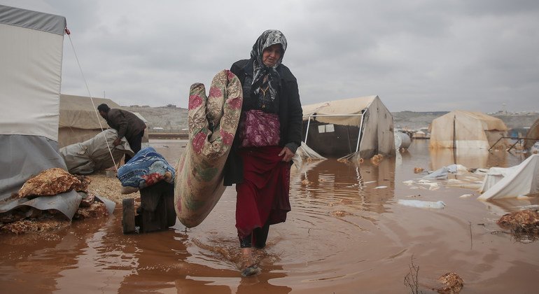 سيّدة تحاول إنقاذ حاجياتها بعد أن أغرقت الفيضانات مخيمها الواقع في شمال غرب سوريا في كانون الثاني/يناير 2021.