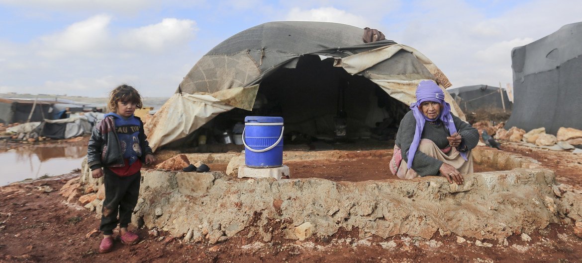 A child stands next to a woman as she makes a makeshift wall to prevent floodwater from entering her tent at an IDP camp in north-west Syria, in January 2021.