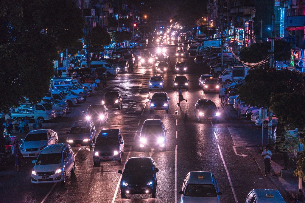 Une rue animée de Yangon, au Myanmar, la nuit, avec de la circulation sur une chaussée mouillée.