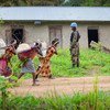 A UN peacekeeper stands guard near an abandoned house as three women carry bundles on a dirt road in Beni, North Kivu.