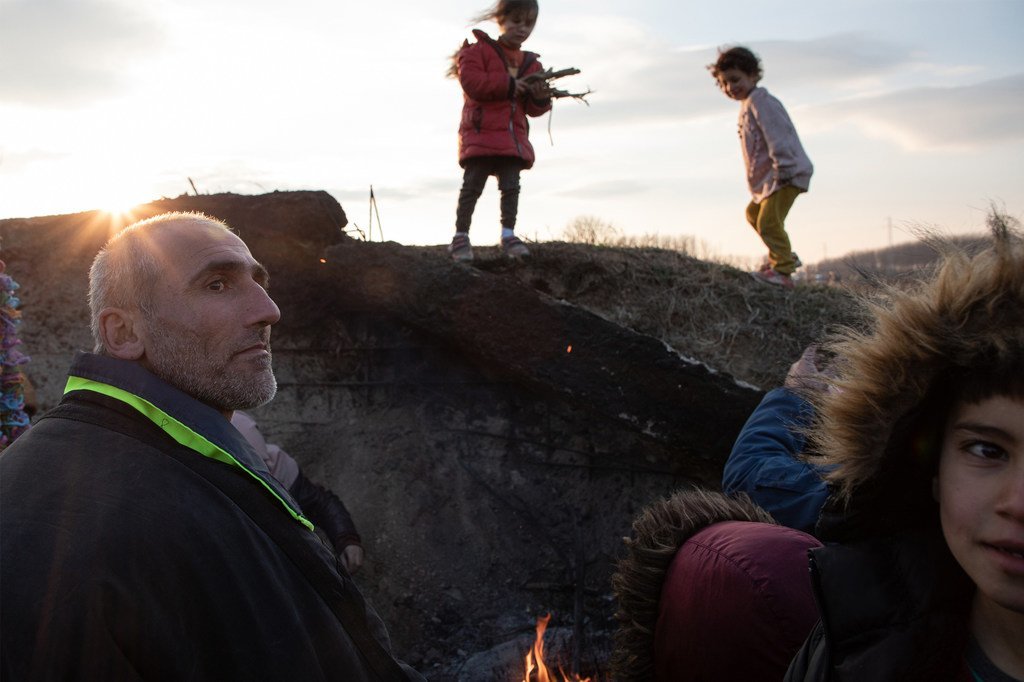 Erdine, nord-ouest de la Syrie. Une famille syrienne se protège du vent à la tombée de la nuit. Les enfants ramassent des branches pour faire un feu de camp tandis que les adultes réfléchissent à leurs options après avoir échoué à entrer en Grèce.