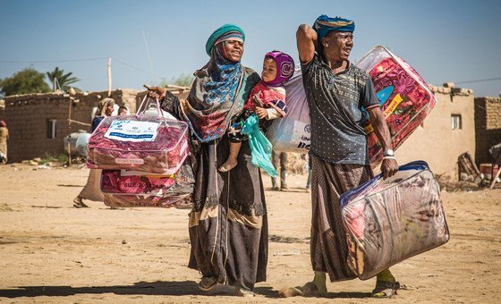 A displaced family in Marib, Yemen, carries a winter aid package back to their shelter.