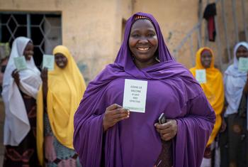 سيدة تبتسم وهي تحمل بطاقة التطعيم ضد كوفيد-19 في نيجيريا.