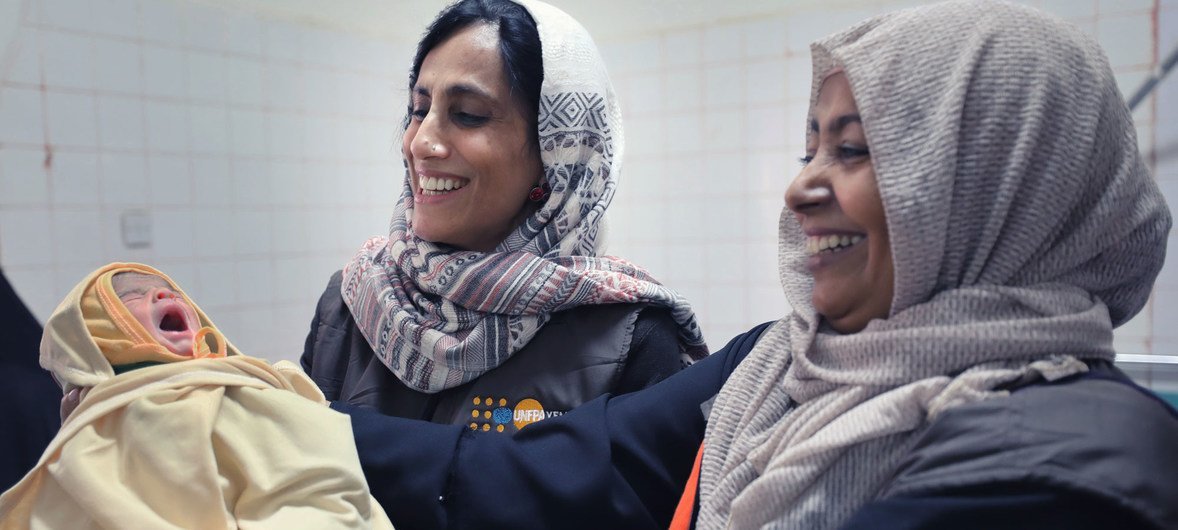 من اليمين: الدكتورة أفراح ثابت الأديمي، أخصائية برامج الصحة الإنجابية بمكتب صندوق الأمم المتحدة للسكان في اليمن، تحمل طفلا حديث الولادة في مستشفي في اليمن.