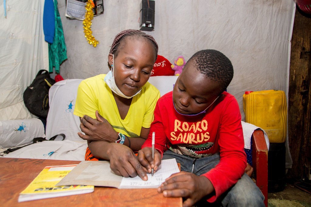 Un garçon de dix ans étudie avec l'aide de sa mère à la maison dans le quartier informel de Mathare à Nairobi, au Kenya.