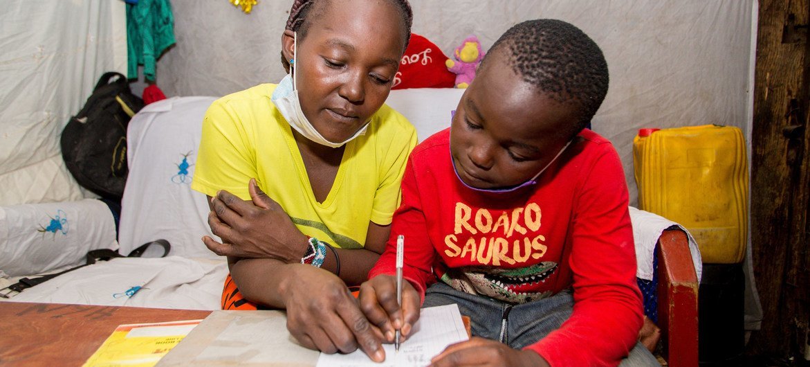 صبي في العاشرة من عمره يدرس بمساعدة والدته في المنزل في ماثاري، بنيروبي، كينيا.