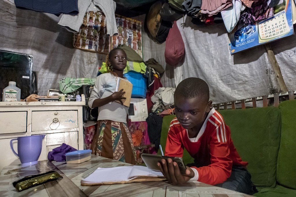 Samuel, 11 ans, et sa sœur Janet, 10 ans, étudient à l'unique table de leur maison à Mathare, Nairobi, Kenya, en utilisant le téléphone portable de la famille