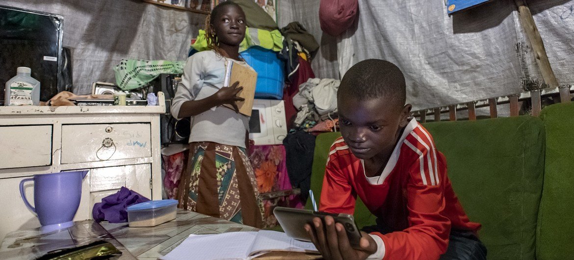 Samuel, 11 ans, et sa sœur Janet, 10 ans, étudient à l'unique table de leur maison à Mathare, Nairobi, Kenya, en utilisant le téléphone portable de la famille