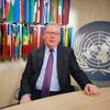 UNDP驻华代表尼古拉斯·罗塞利尼坐在办公桌前，背景是联合国徽标和国际旗帜。