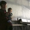 طفلة تحمل طفلا صغيرا وتجلس على مقعد في مدرسة تحولت إلى ملجأ في شمال الرقة في سوريا.