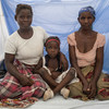 Au Mozambique, trois générations d'une famille assises ensemble sur un lit protégé par une moustiquaire imprégnée.