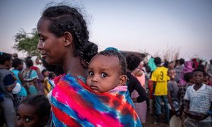 一名从埃塞俄比亚提格雷抵达苏丹的难民背着孩子等待领取食品。