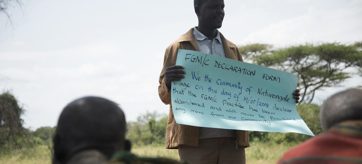 A man holds up a declaration that reads that the Naturongole village, in Uganda, has abandoned FGM/C and that it will never be practiced in the community.