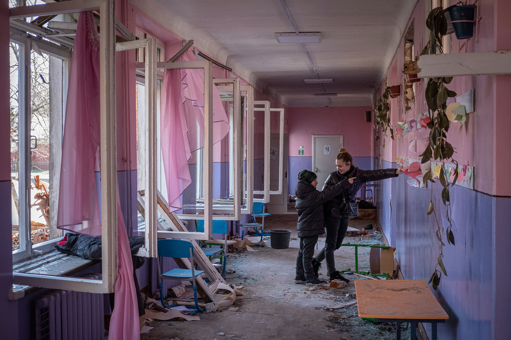 Unos niños miran los trabajos de arte en un aula sembrada de cristales rotos y otros escombros en Chernihiv, Ucrania.