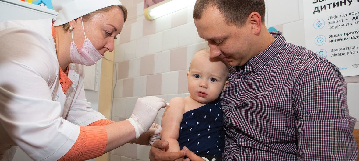 Un padre sostiene a su niño mientras una enfermera le administra una vacuna.