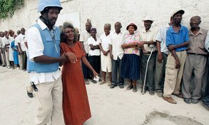Bibi anasaidiwa kutembea ili afike kwenye kibanda cha kupiga kura mnamo 2006, huko Port-au-Prince, na afisa wa polisi wa Umoja wa Mataifa.