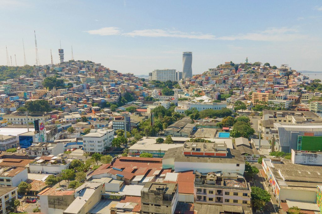 Vista aérea de Guayaquil, Ecuador, que muestra un denso paisaje urbano con coloridos edificios en las laderas y modernos rascacielos en el centro.