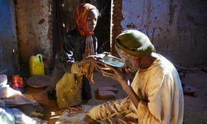 A seven-year-old girl gives water to her grandfather while he prays in a camp for internally displaced people in Darfur, Sudan.