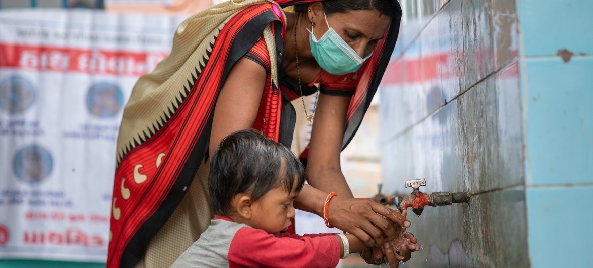 भारत के गुजरात में स्वच्छता और कोविड महामारी की रोकथाम के लिये एक सामुदायिक स्वास्थ्य कार्यकर्ता, एक बच्चे को सही ढंग से हाथ धोना सिखाते हुए.