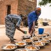 Mothers are dishing out the freshly prepared school lunch onto large plates in Niger