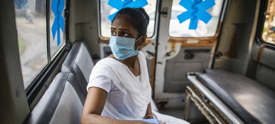 गुजरात में एक दाई नीलम बामनिया, एक सार्वजनिक स्वास्थ्य केन्द्र के कोविड-19 टीकाकरण सत्र के लिये टीके लेने के लिये एम्बुलेन्स में जा रही हैं. कोविड टीकों को वैक्सीन के नीले डब्बों में ले जाया जाता है.