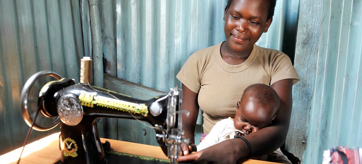 केनया में एक महिला अपने बच्चे की देखभाल करते हुए ही, सिलाई का काम करते हुए.