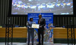 Téné Maïmouna Zoungrana reçoit le Prix de la Pionnière des Nations Unies des mains du Chef de cabinet du Secrétaire général Courtenay Rattray.