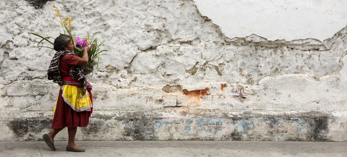 Una mujer carga una cesta de flores por las calles empedradas y los muros derruidos de Antigua, en Guatemala.