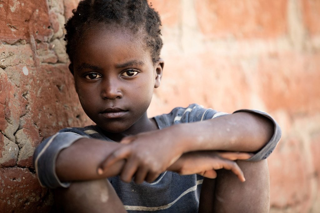 Um menino com HIV está sentado encostado em uma parede de tijolos na Zâmbia.