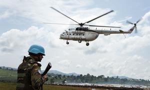 A UN blue helmet from the MONUSCO peacekeeping mission stands guard as a UN helicopter delivers aid and humanitarian personnel to Rhoe IDP camp, Ituri, Democratic Republic of the Congo.