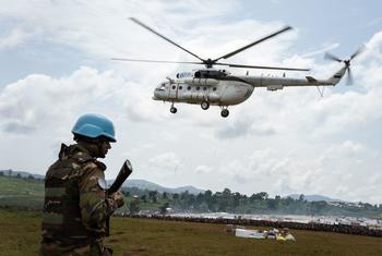 एक यूएन हैलीकॉप्टर काँगो लोकतांत्रिक गणराज्य (DRC) में देश के भीतर विस्थापित लोगों के लिये बनाए गए इतूरी शिविर में राहत सामग्री लाते हुए. पास ही एक यूएन शान्तिरक्षक चौकसी पर.