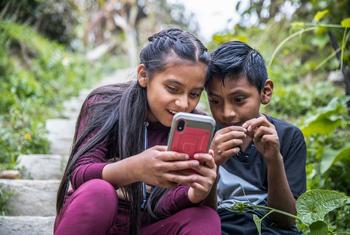 Dos niños juegan con su teléfono al aire libre mientras sus padres participan en un taller sobre seguridad en la red y prácticas parentales positivas, en Guatemala.